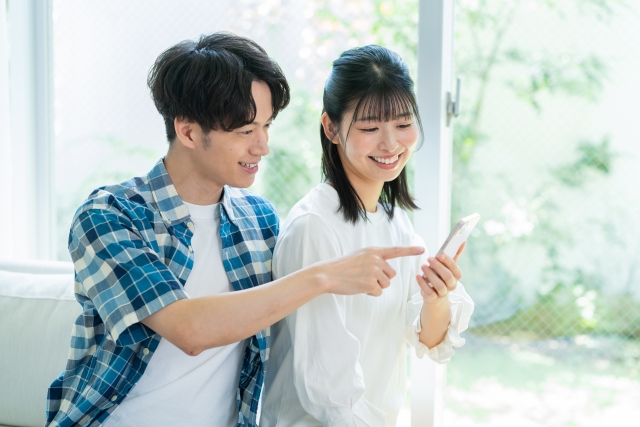 ソファで笑顔の夫婦がスマートフォンを見ている写真