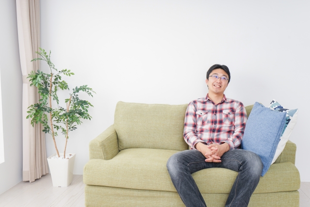 ソファに座って笑顔でくつろぐ男性の写真