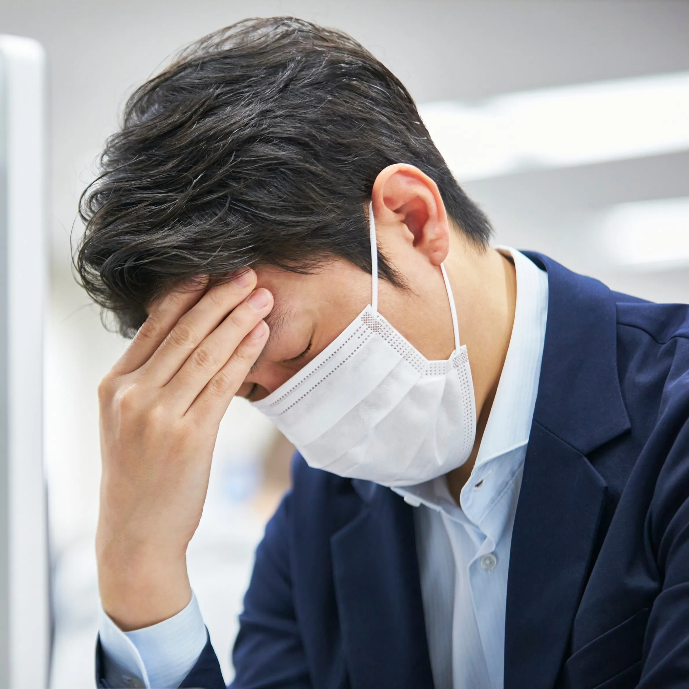 マスクを着けて頭を抱える男性の写真