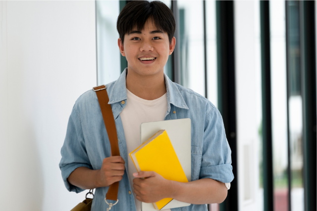 ノートを持って笑顔で立つ男性の写真