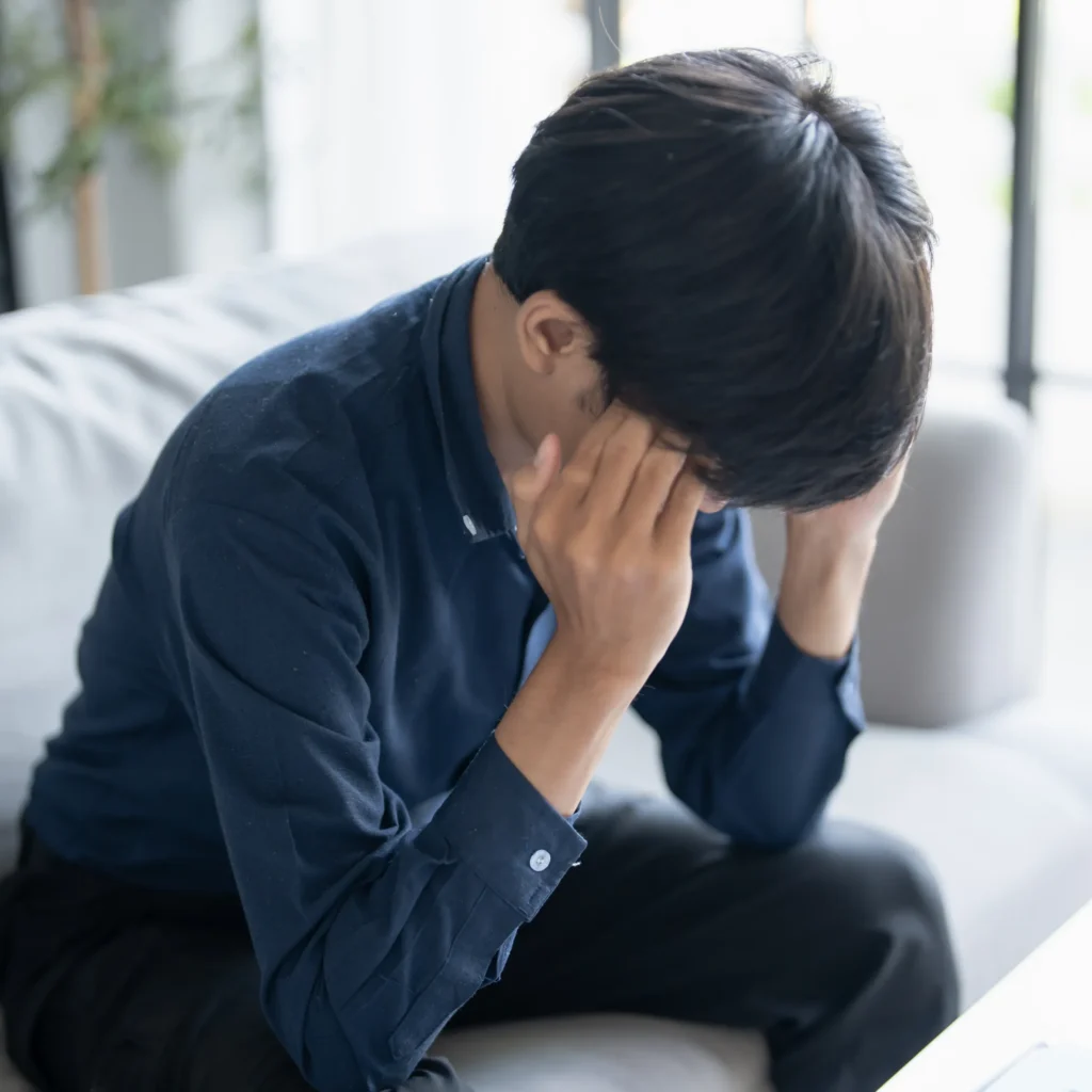ソファで頭を抱えて悩む男性の写真